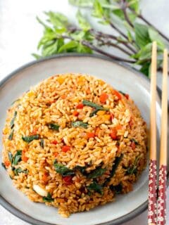 thai basil fried rice in a bowl mold on top of a grey ceramic plate with wooden chopsticks and thai basil next to the plate