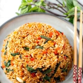 thai basil fried rice in a bowl mold on top of a grey ceramic plate with wooden chopsticks and thai basil next to the plate