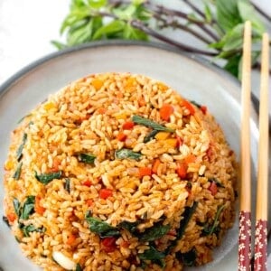 thai basil fried rice in a bowl mold on top of a grey ceramic plate with wooden chopsticks and thai basil next to the plate