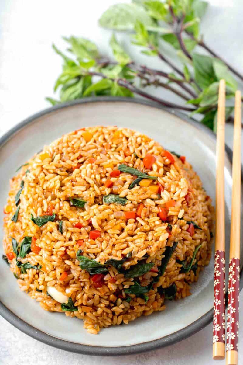 thai basil fried rice in a bowl mold on top of a grey ceramic plate with wooden chopsticks and thai basil next to the plate