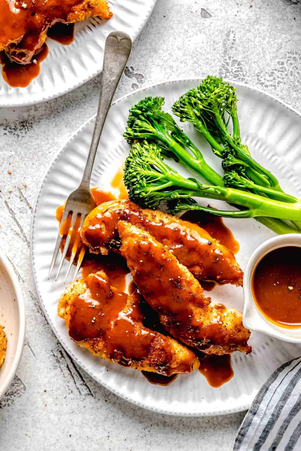 Closeup of bourbon chicken on a plate with broccoli, extra sauce, and a fork.
