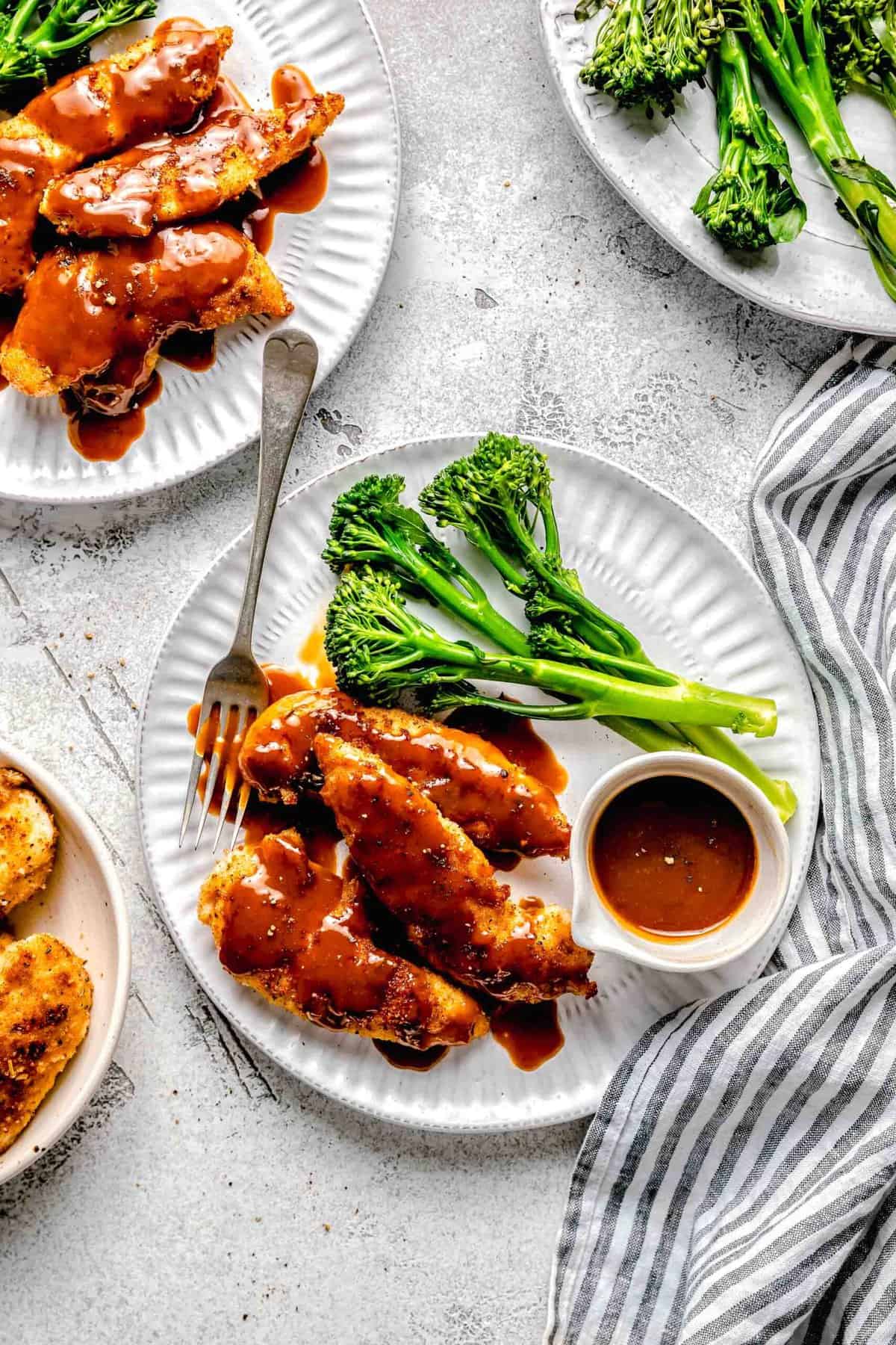 Bourbon chicken on a plate with broccoli, extra sauce, and a fork.