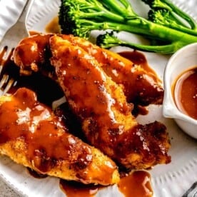 Closeup of bourbon chicken on a plate with broccoli, extra sauce, and a fork.