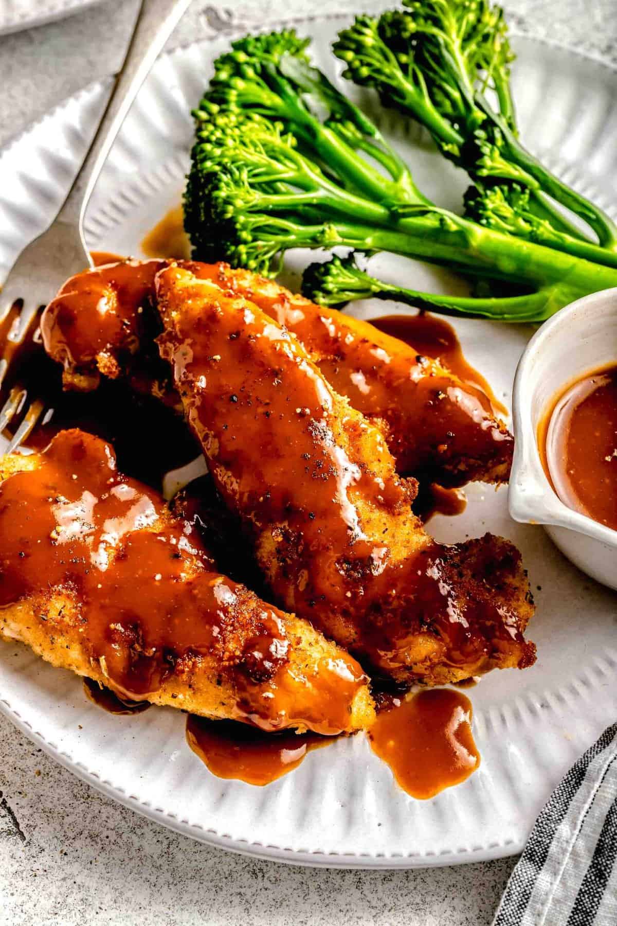Closeup of bourbon chicken on a plate with broccoli, extra sauce, and a fork.