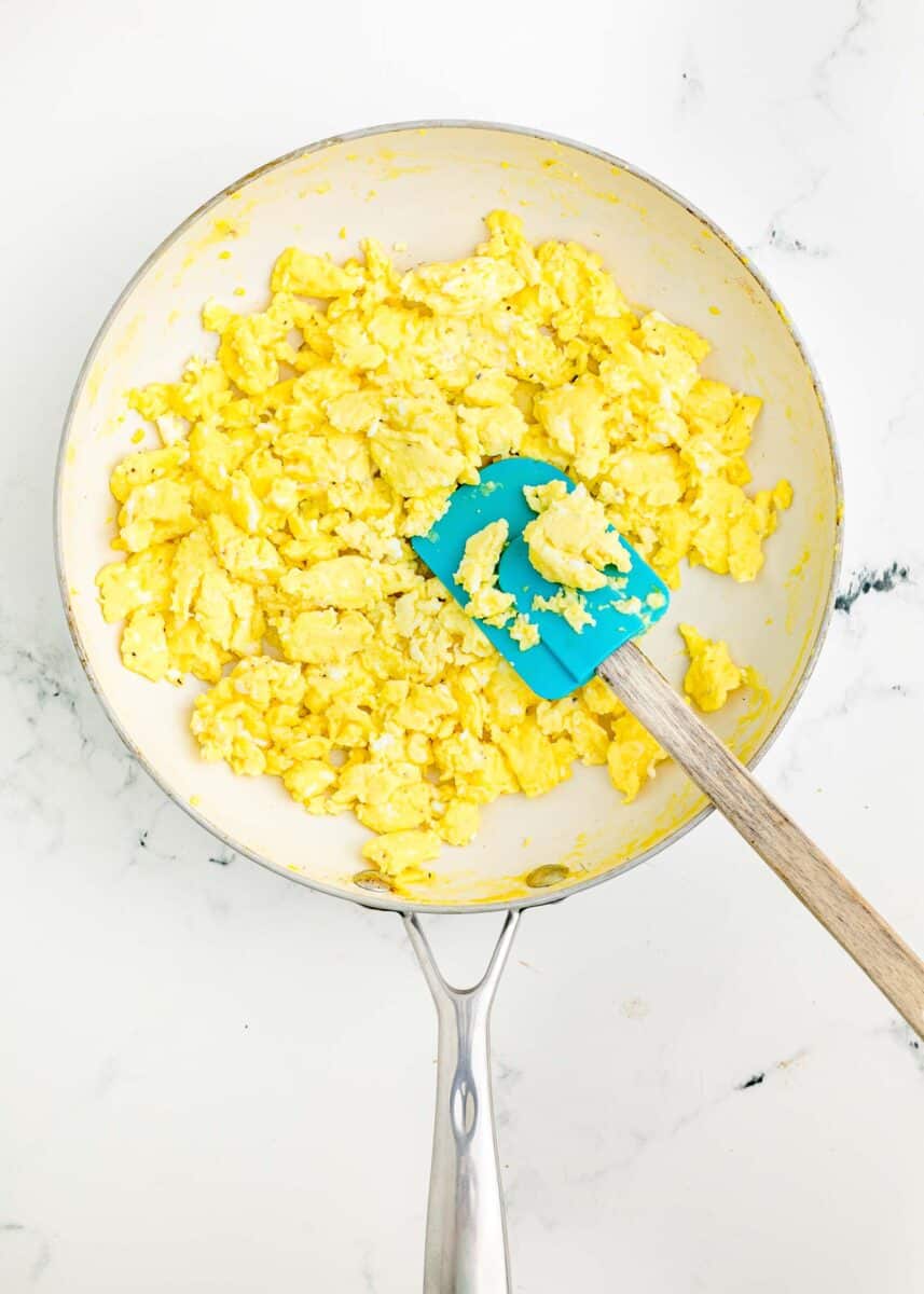 scrambled eggs are being cooked in a skillet with a rubber spatula.