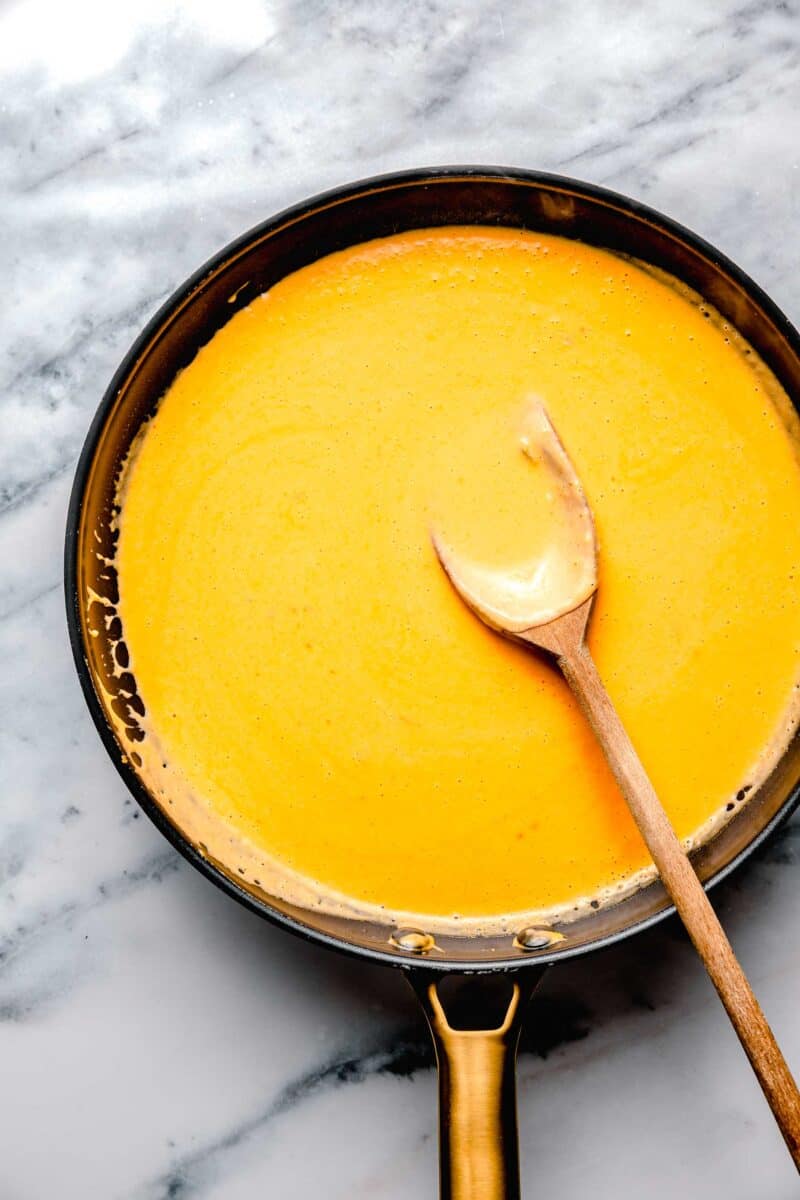 cheese sauce is placed in a skillet with a wooden spoon.