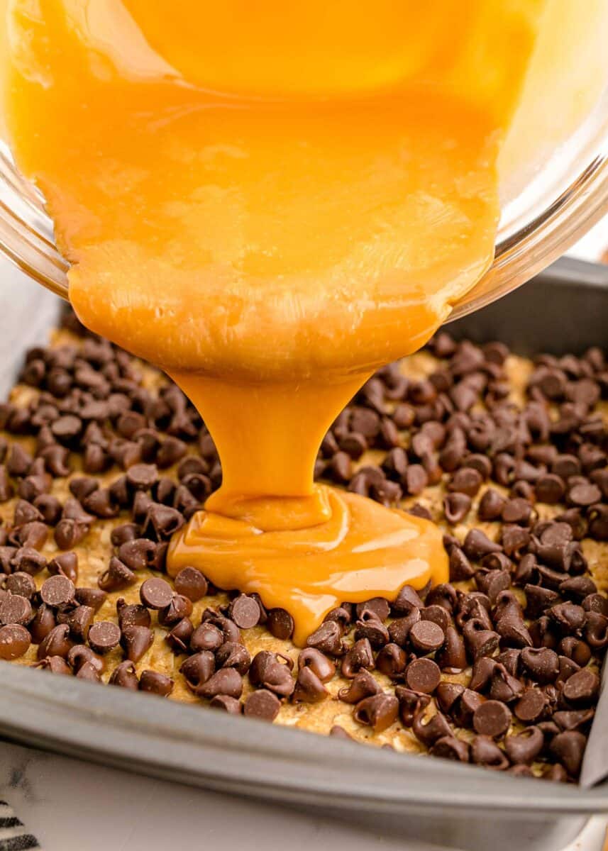caramel sauce is being poured onto a layer of chocolate chips.