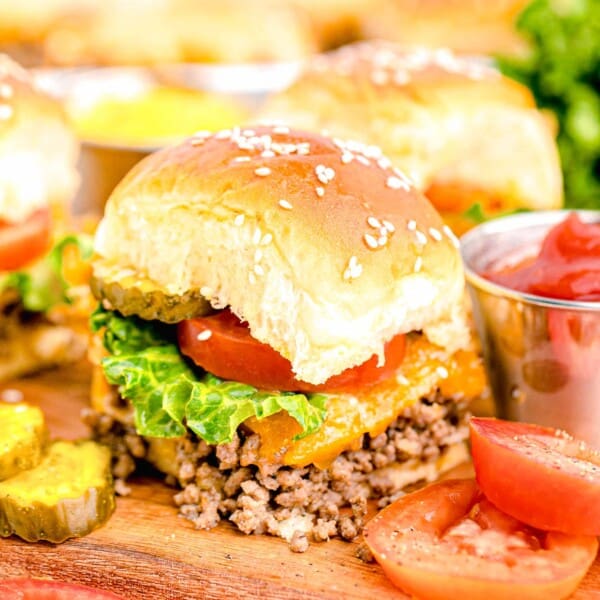 a cheeseburger slider is placed next to sliced pickles and tomatoes.