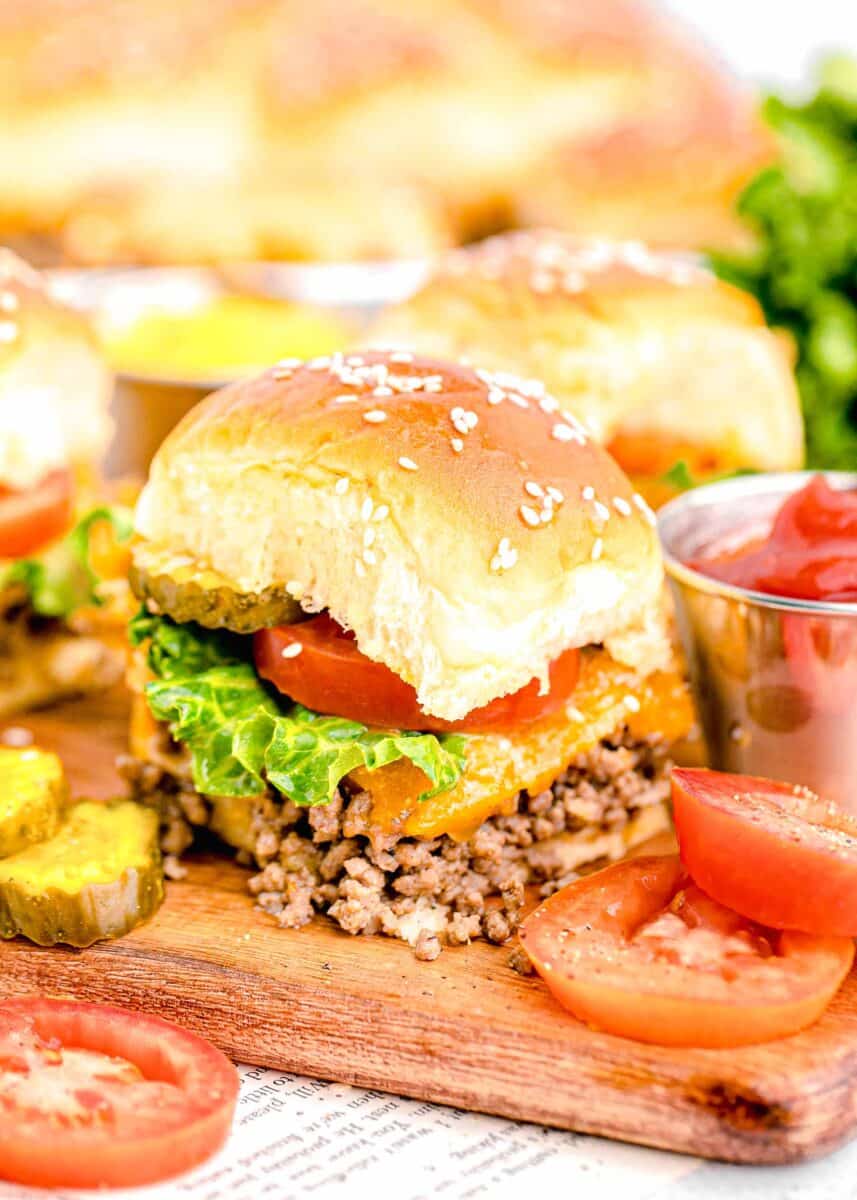 a cheeseburger slider is placed next to sliced pickles and tomatoes.