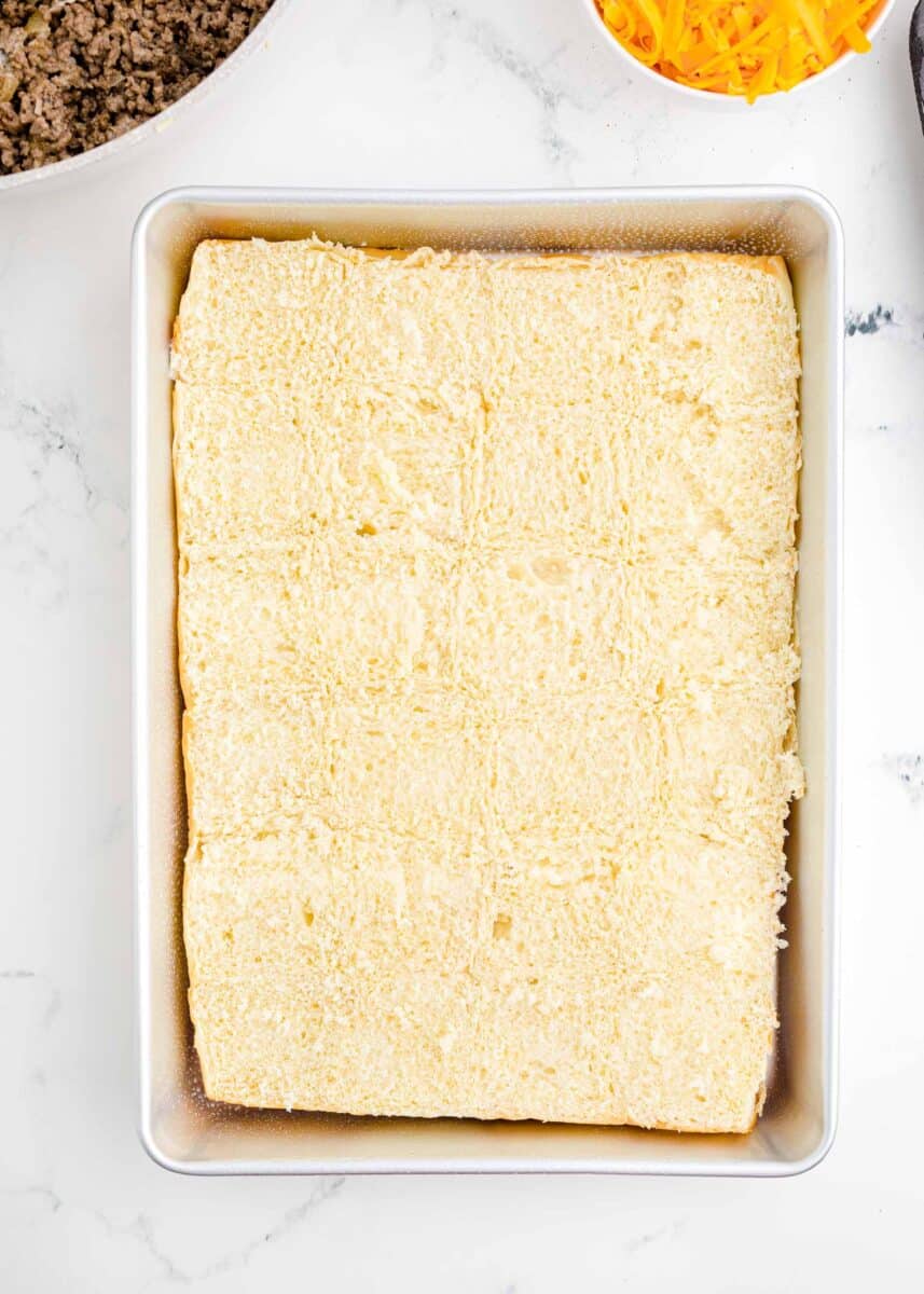 the bottom of a sheet of bread rolls is placed in a baking dish.