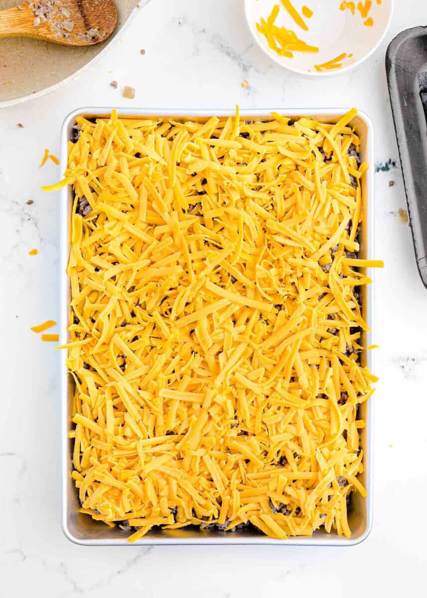 a layer of cheese is placed on top of a layer of cooked ground beef.