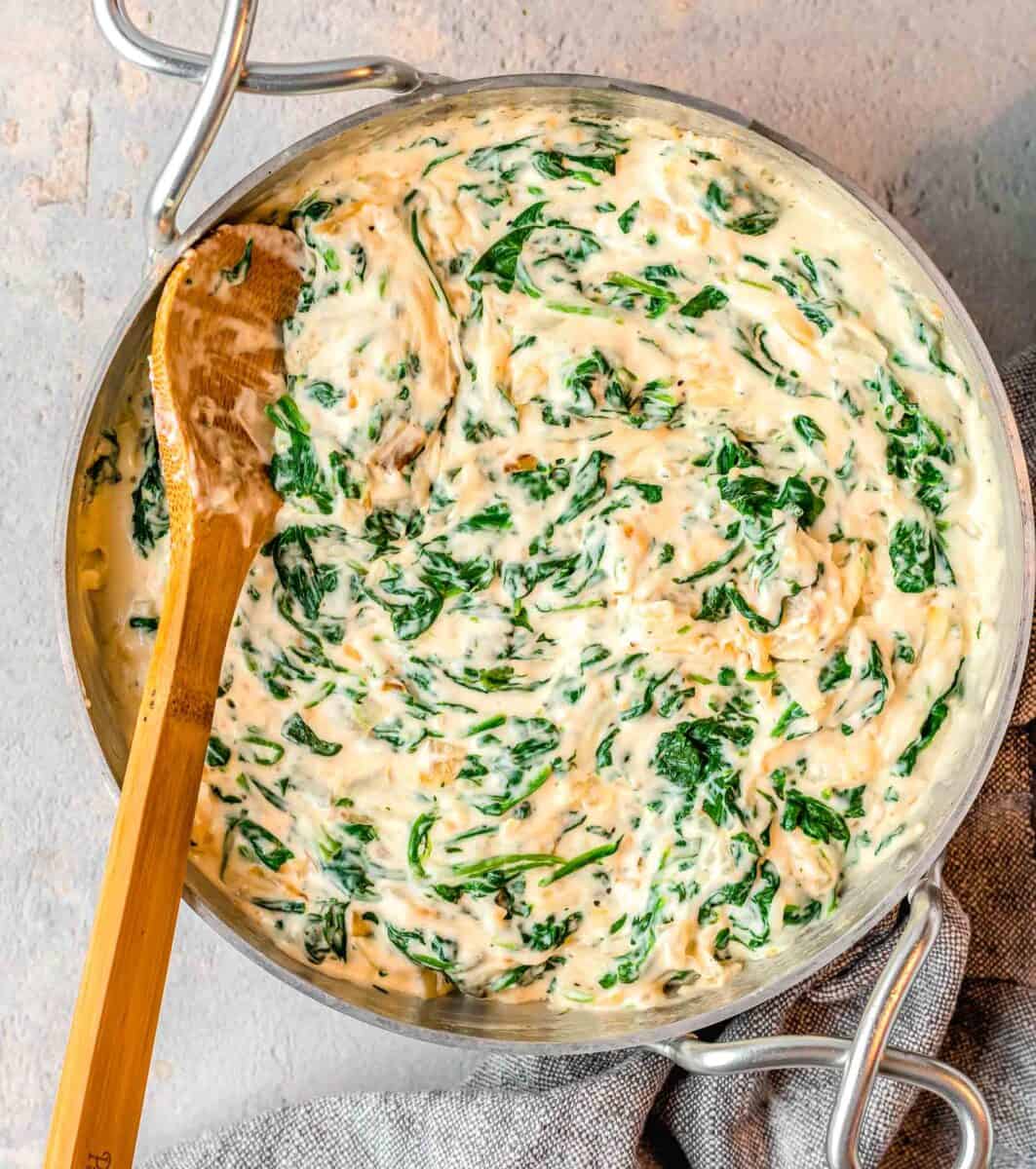 a wooden spoon is stirring cream spinach in a skillet.