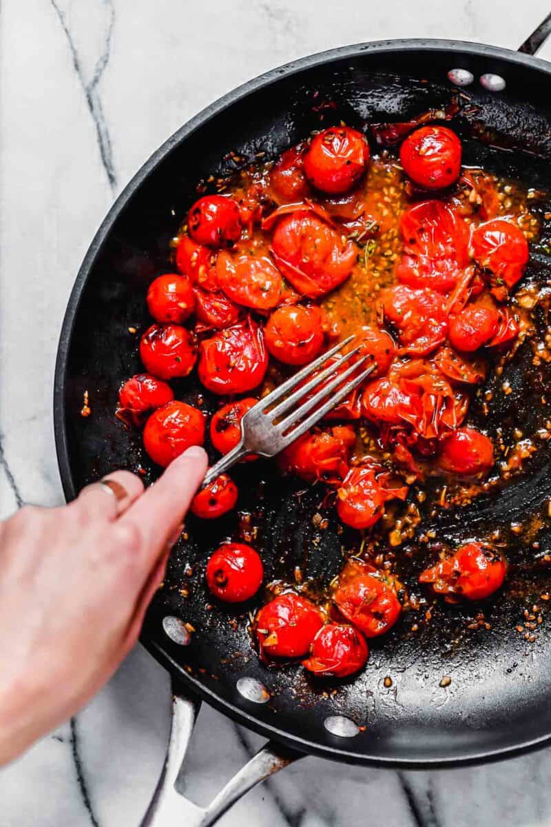 a fork is being used to smash cherry tomatoes in a nonstick skillet