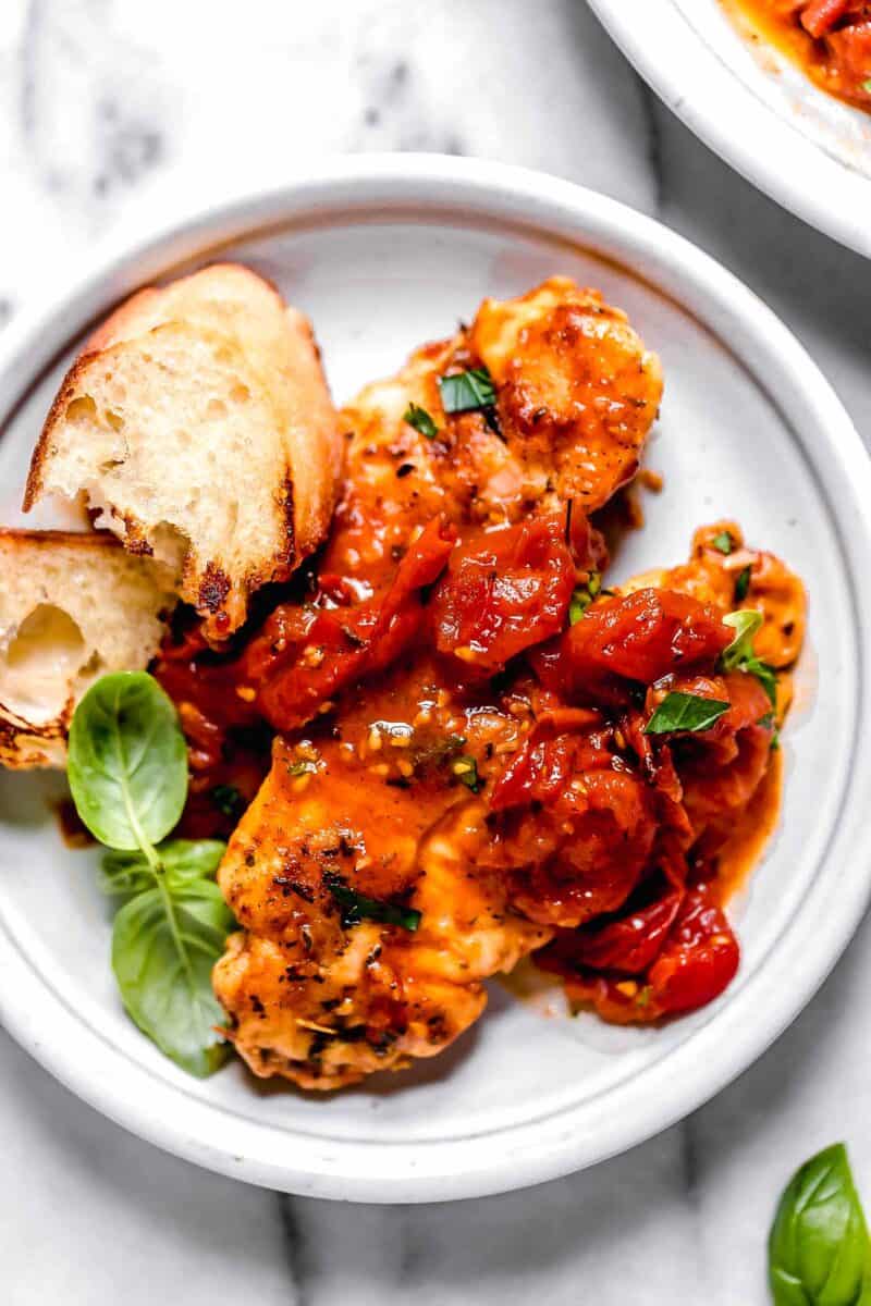 tomato herb pan sauce spread across the top of cooked chicken tenders on a small white plate with toasted bread and fresh basil