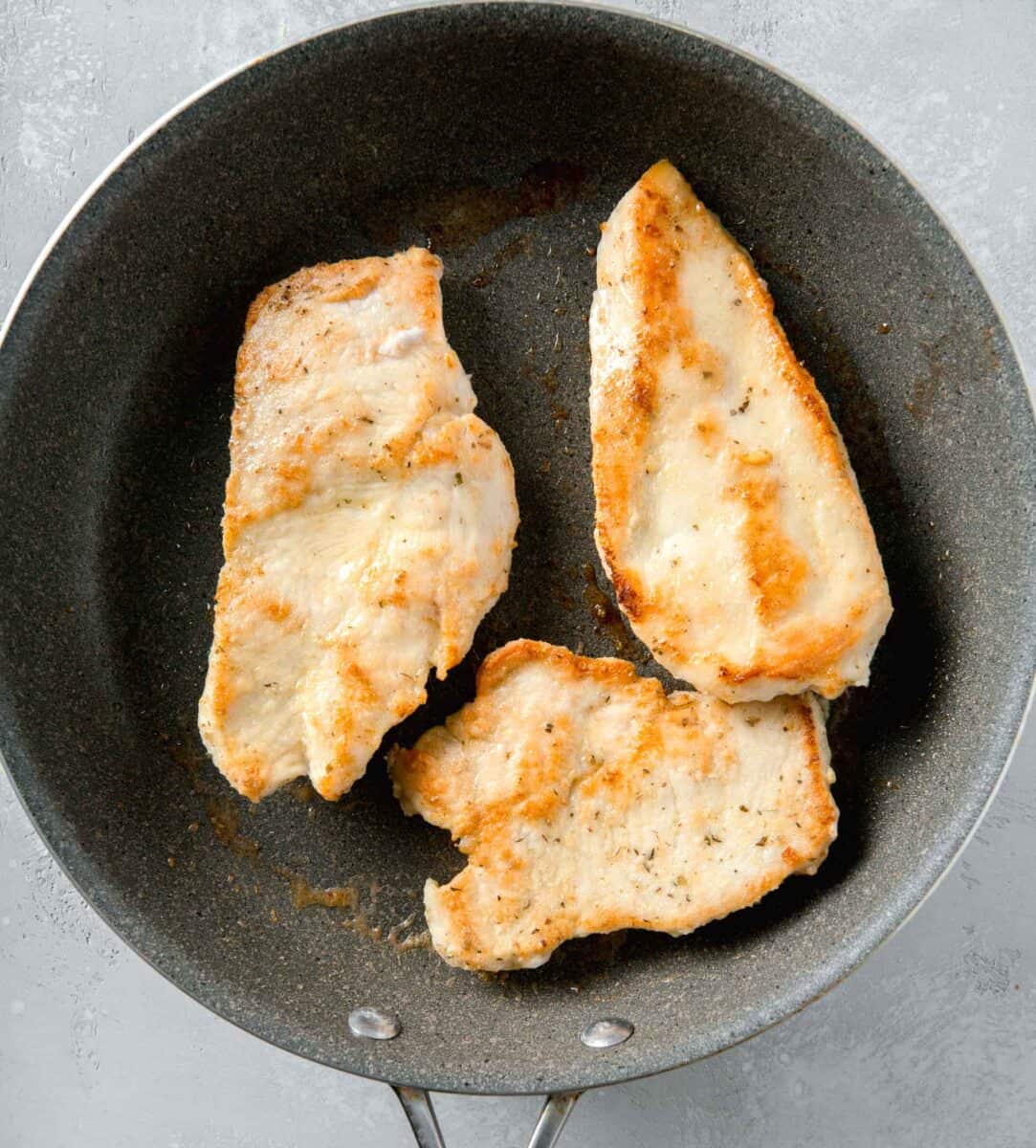 thin cut browned chicken breasts in a large grey nonstick skillet