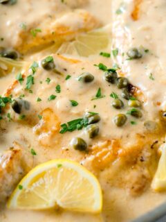 chicken breasts in a creamy lemon sauce with fresh parsley and capers on top next to a lemon wedge