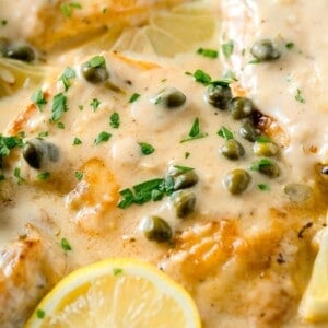 chicken breasts in a creamy lemon sauce with fresh parsley and capers on top next to a lemon wedge
