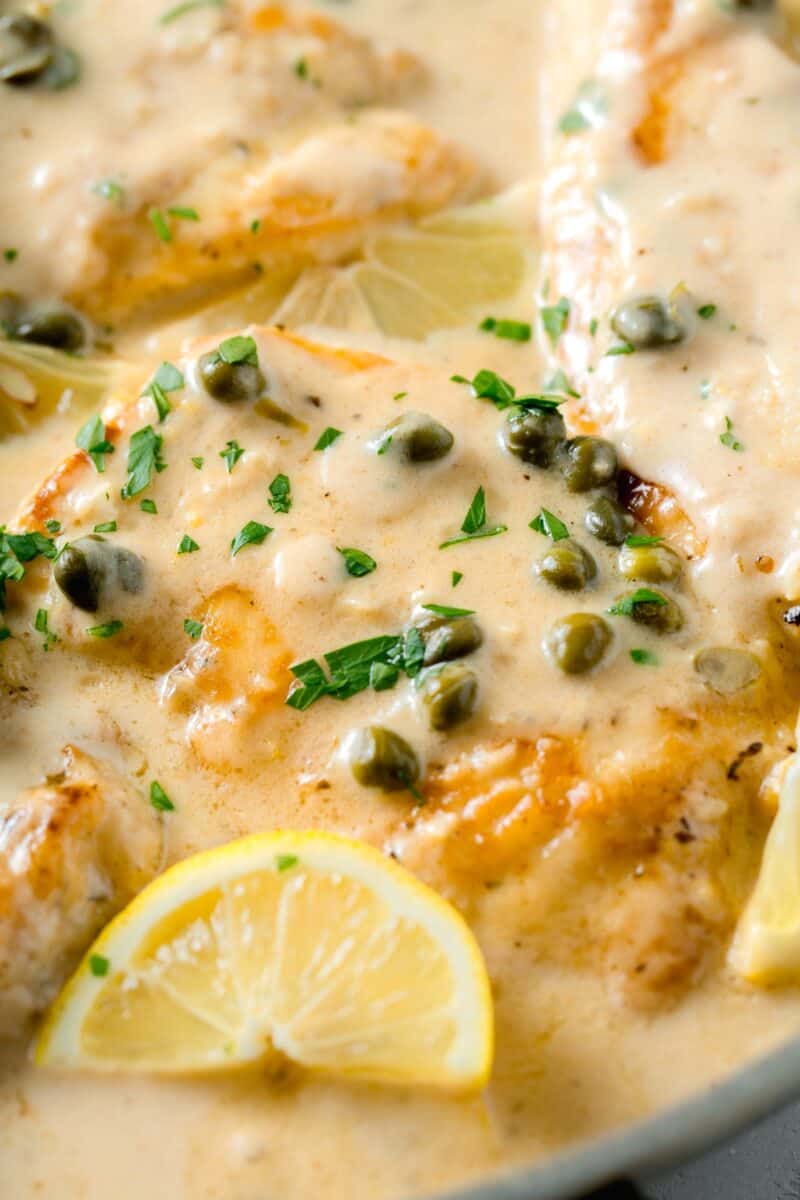 chicken breasts in a creamy lemon sauce with fresh parsley and capers on top next to a lemon wedge