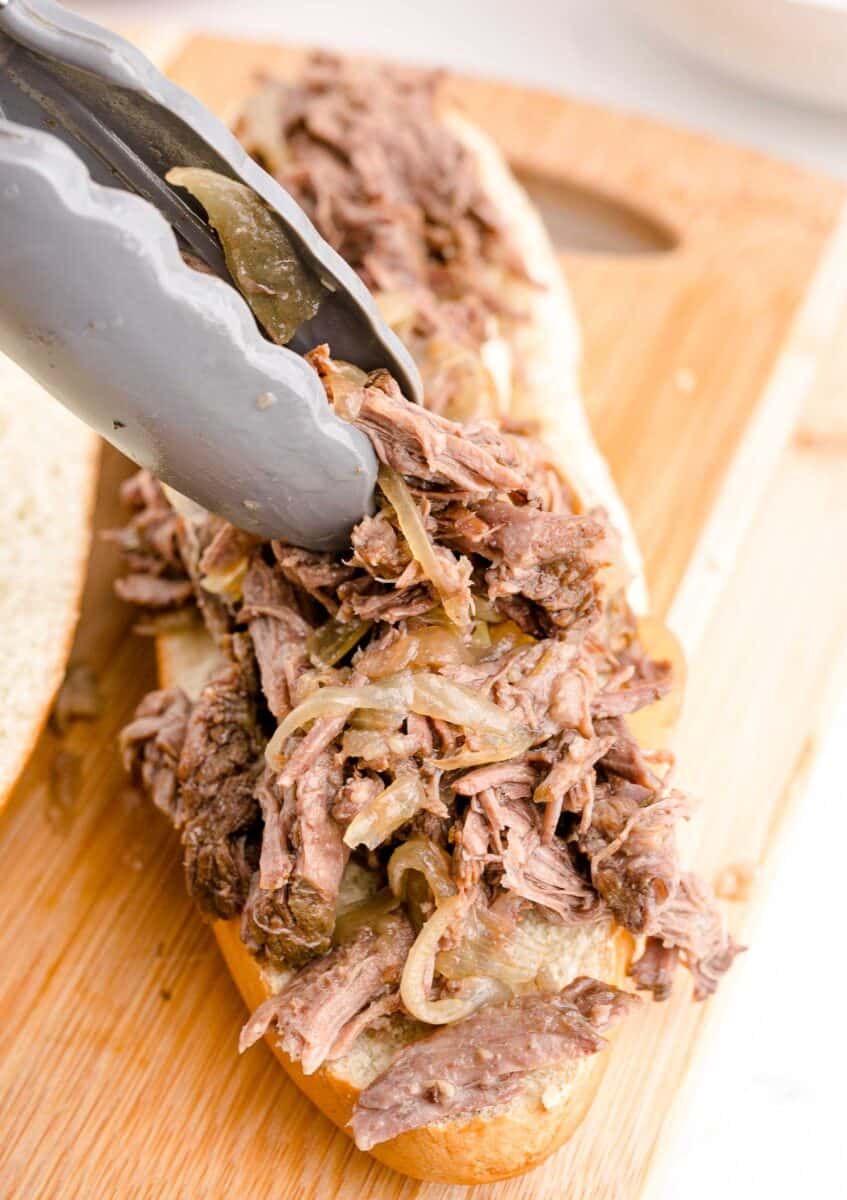 shredded beef is being placed on a loaf of bread.