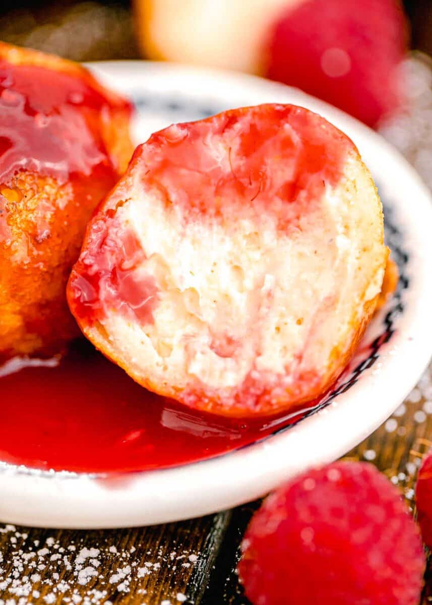 a bite has been taken out of a fried cheesecake bite with raspberry sauce.