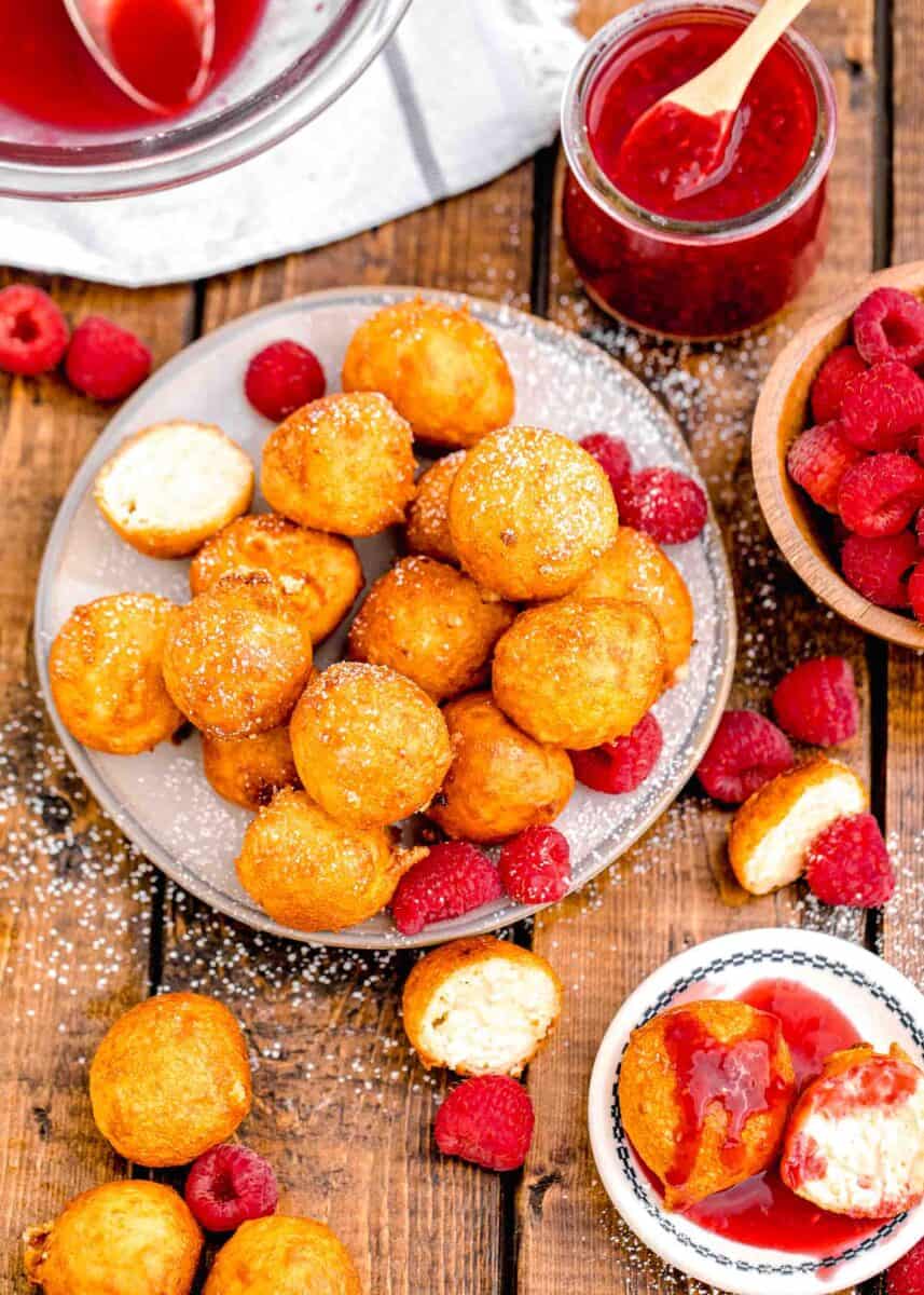 a plate is piled high with fried cheesecake bites and raspberries.