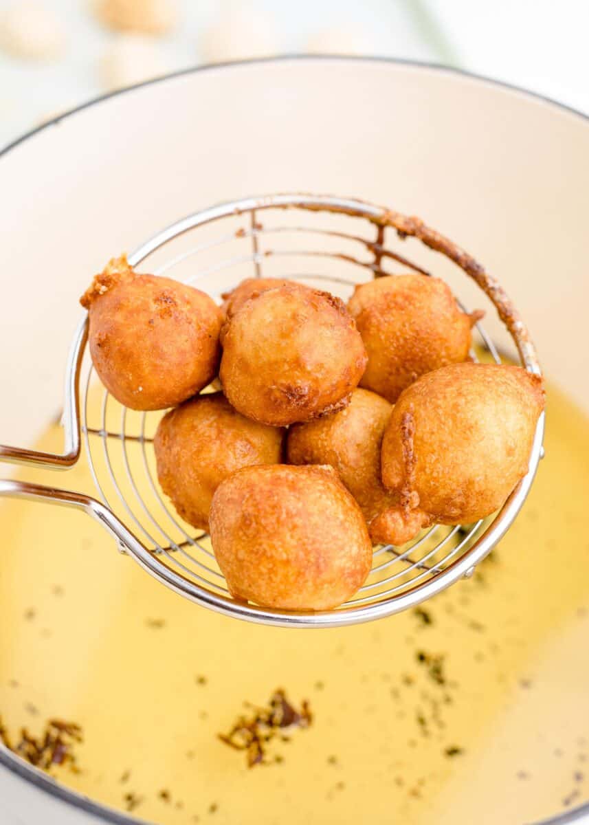 cheesecake bites are being lifted from a pot of hot oil.