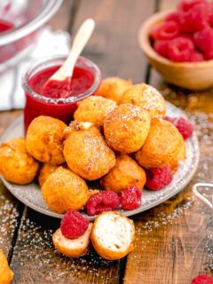 a jar of raspberry sauce is placed next to a plate of fried cheesecake bites.