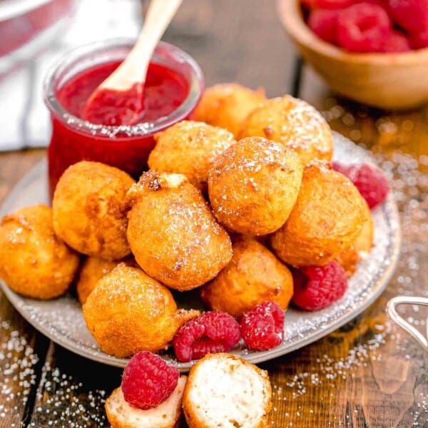 a jar of raspberry sauce is placed next to a plate of fried cheesecake bites.