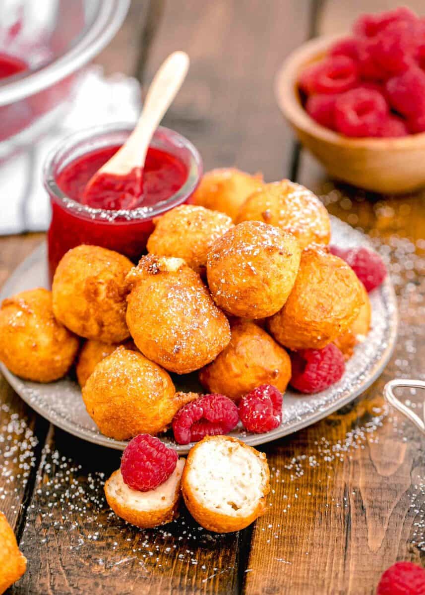 a jar of raspberry sauce is placed next to a plate of fried cheesecake bites.