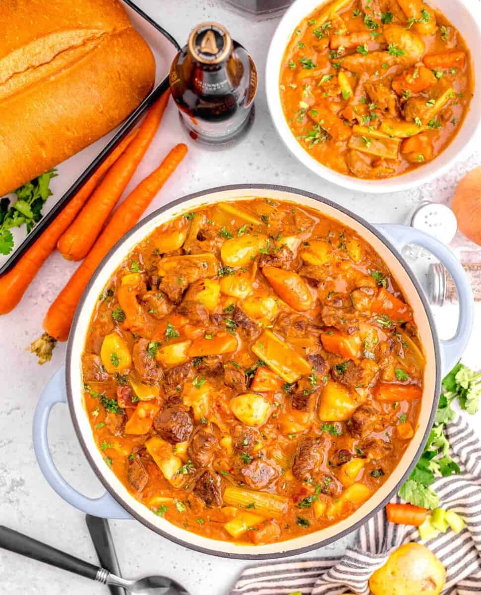 guinness beef stew in a large pot with a bowl of beef stew next to it amongst other ingredients that were used in the stew