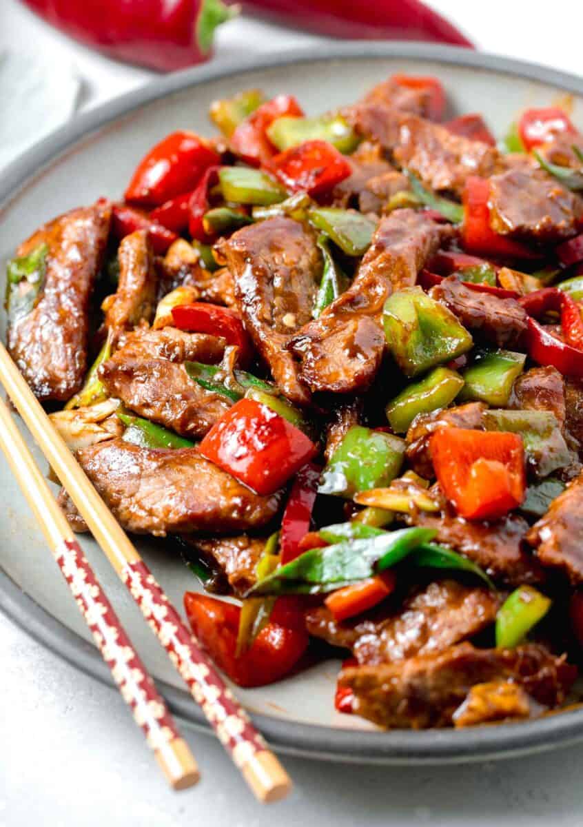 a large plate of hunan beef with wooden chopsticks sitting on the grey ceramic plate