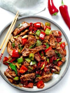 overhead image of large plate of hunan beef with wooden chopsticks next to fresno peppers and green linen towel