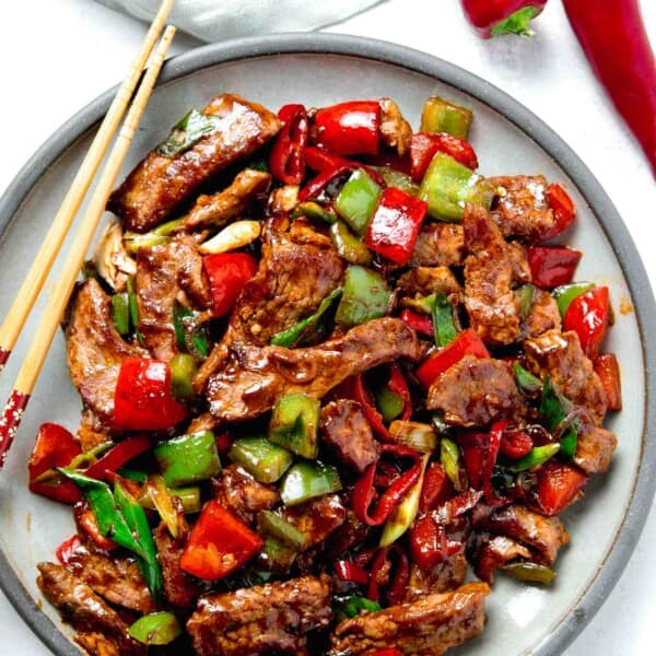 overhead image of large plate of hunan beef with wooden chopsticks next to fresno peppers and green linen towel