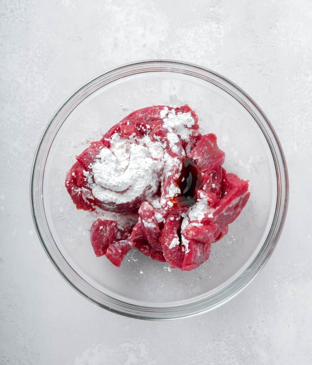 raw strips of flank steak in a clear bowl with cornstarch and oyster sauce