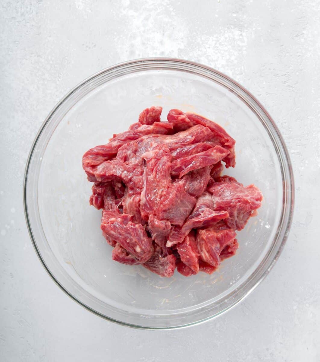raw flank steak pieces mixed up with cornstarch in a clear bowl