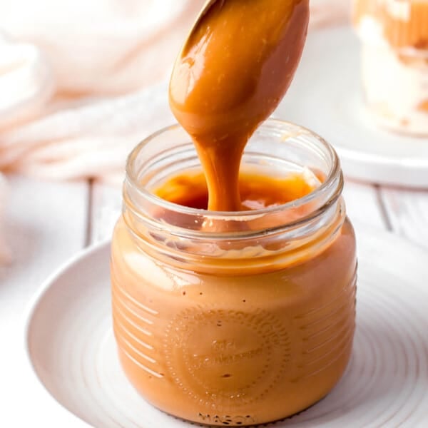 a spoon is drizzling dulce de leche into a jar.