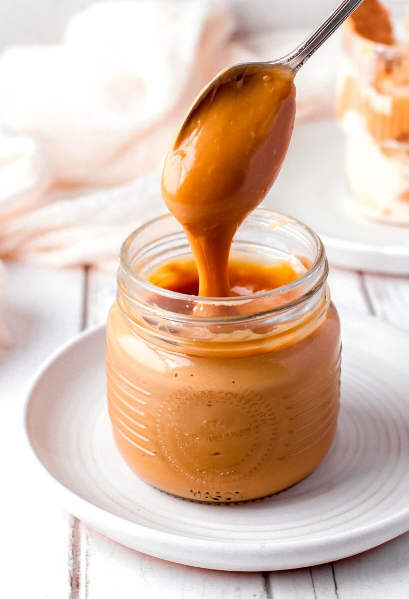 a spoon is drizzling dulce de leche into a jar.