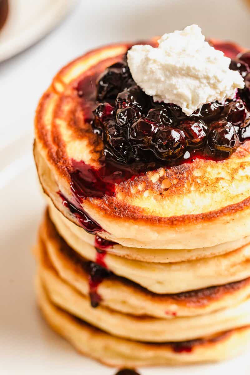blueberries and whipped cream are placed on top of a stack of lemon ricotta pancakes.