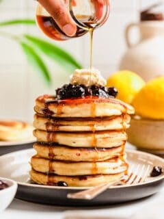 maple syrup is being drizzled on top of a stack of pancakes.