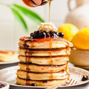 maple syrup is being drizzled on top of a stack of pancakes.