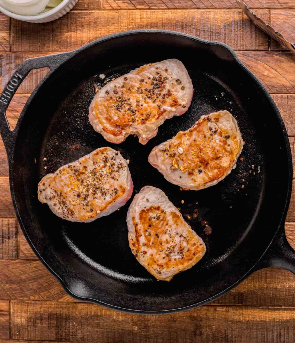 pork chops are being seared in a black skillet.