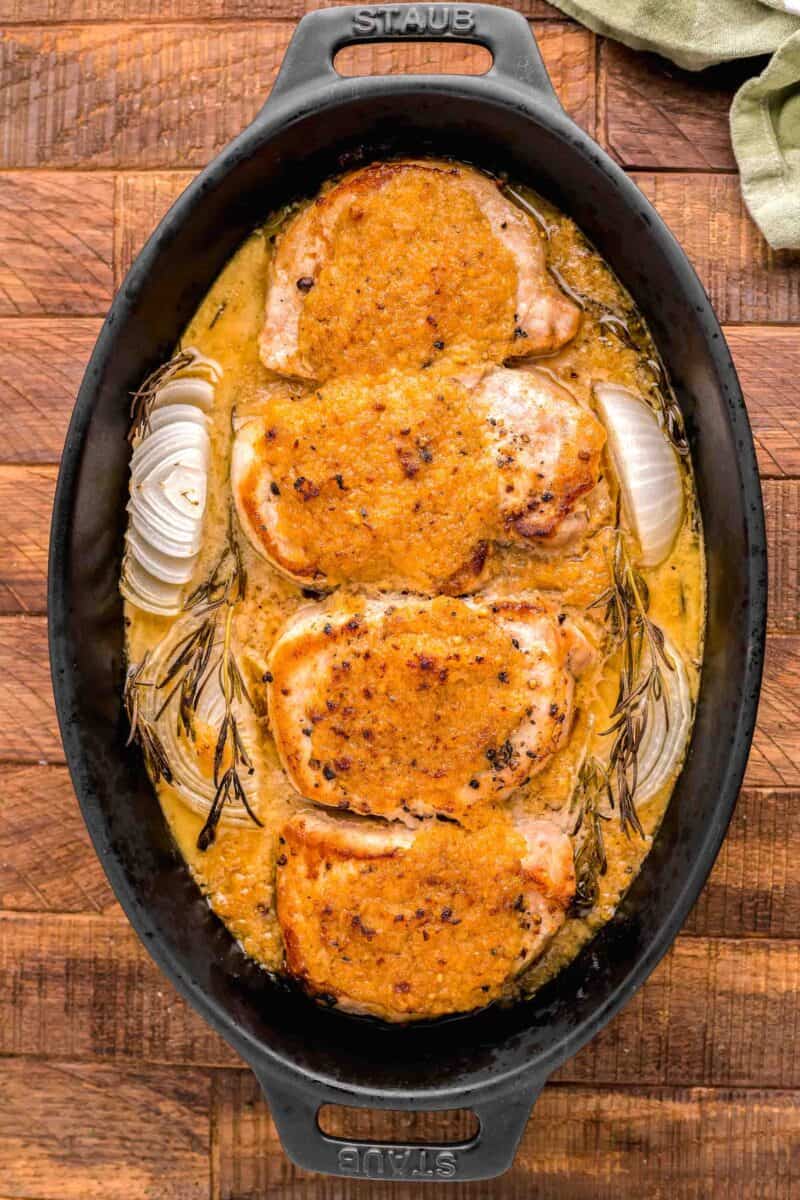 four pork chops are set next to each other in a black pot.