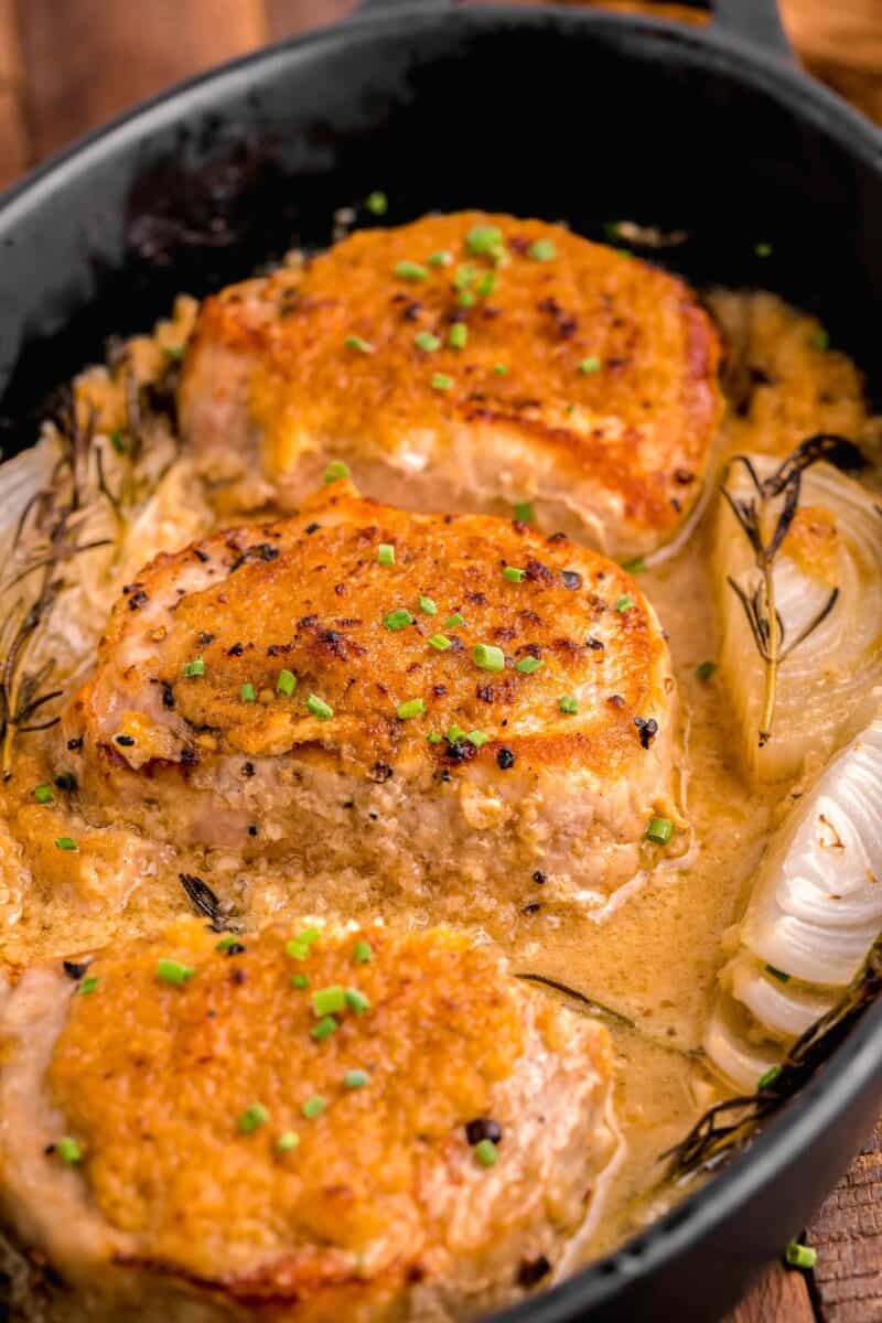 several pork chops are presented in a pot with onions and herbs.