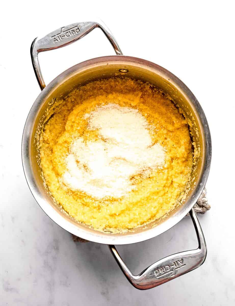 Adding parmesan cheese to cooked polenta in a pot.