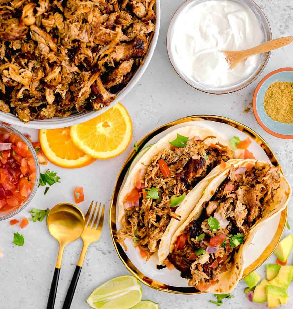 two tacos are placed next to a skillet filled with carnitas meat.