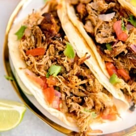 two tacos are garnished and plated next to limes and oranges.