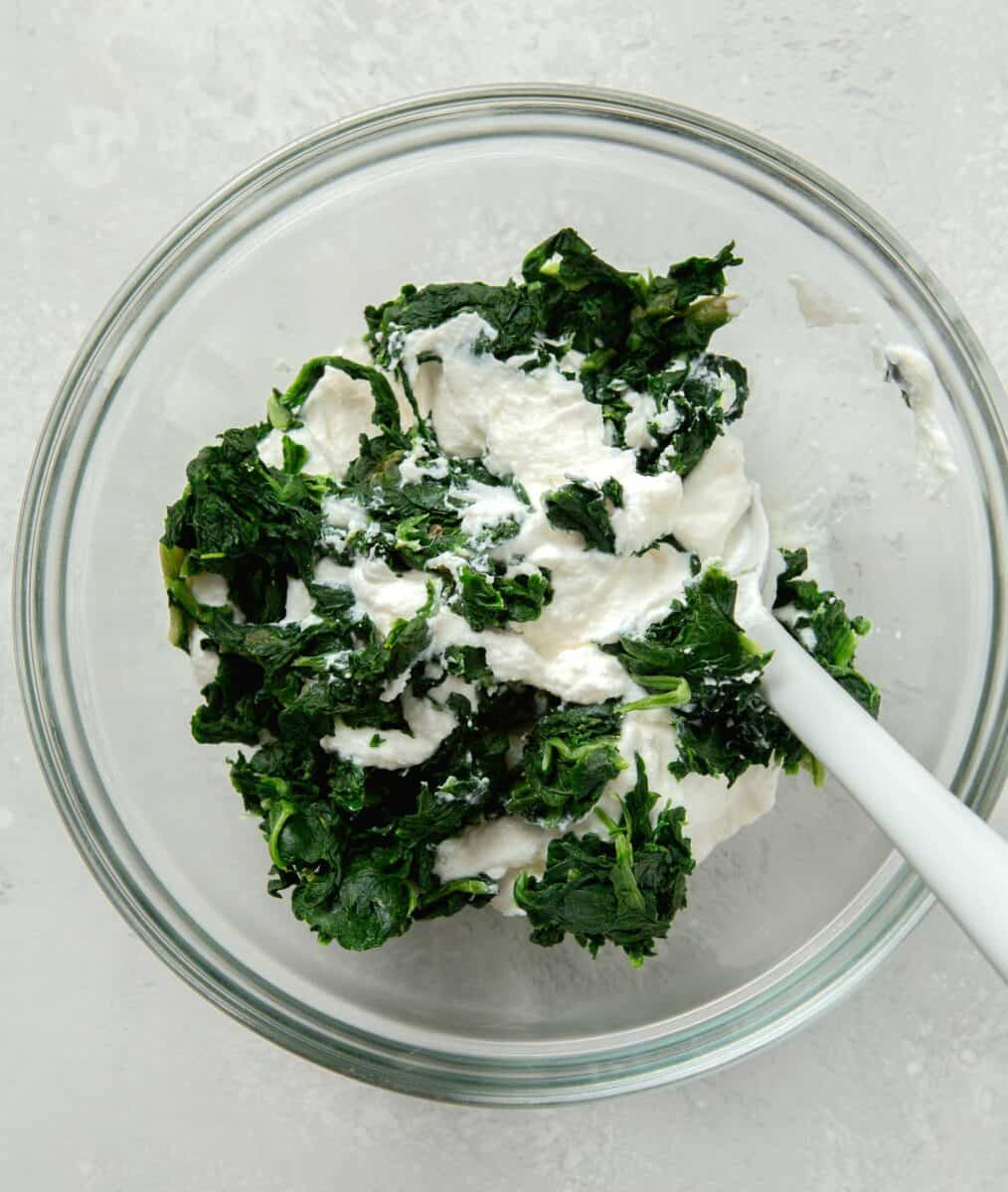 ricotta and spinach in a clear bowl with a silicone spoon