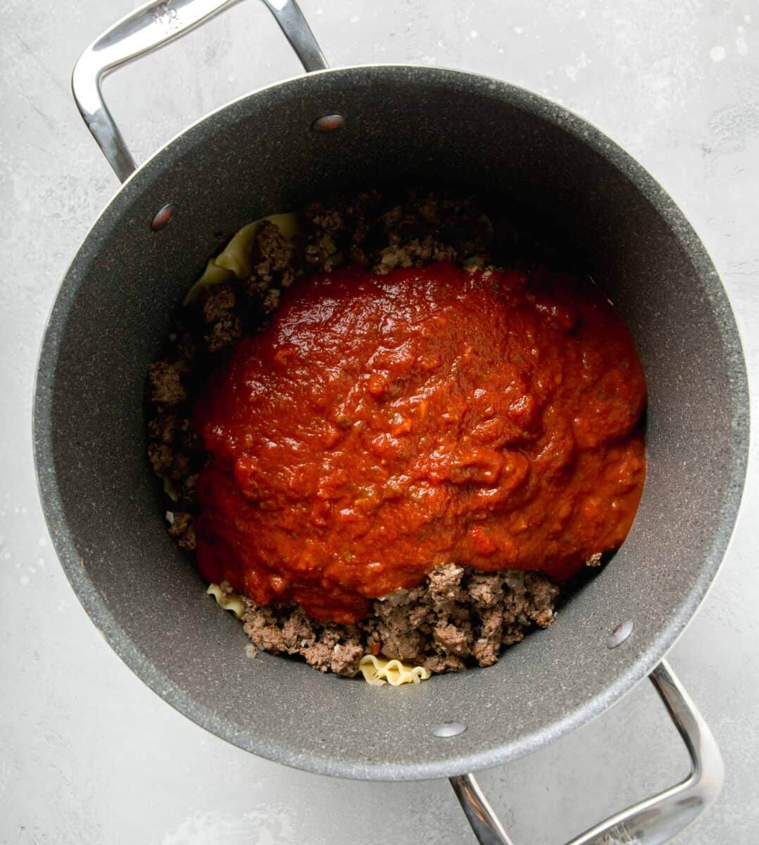 marinara sauce on top of ground beef mixture and lasagna noodles in a large pot