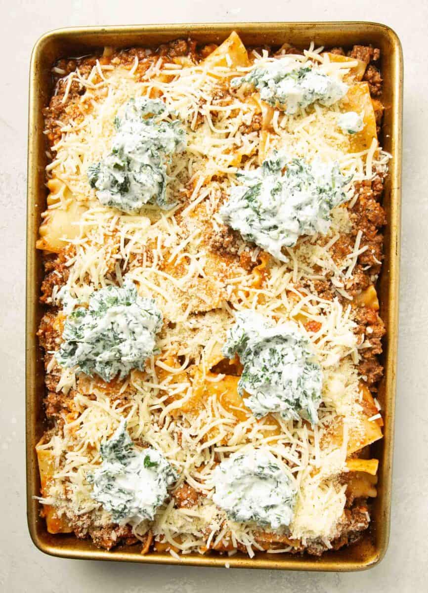 assembled sheet pan lasagna on a metal rimmed baking sheet with ricotta and spinach dollops on top