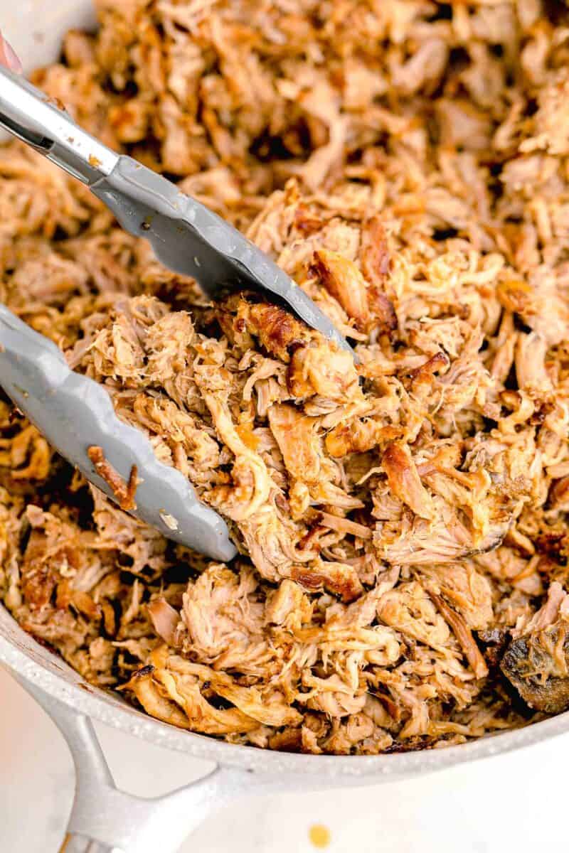 tongs are placed in a bowl of carnitas.